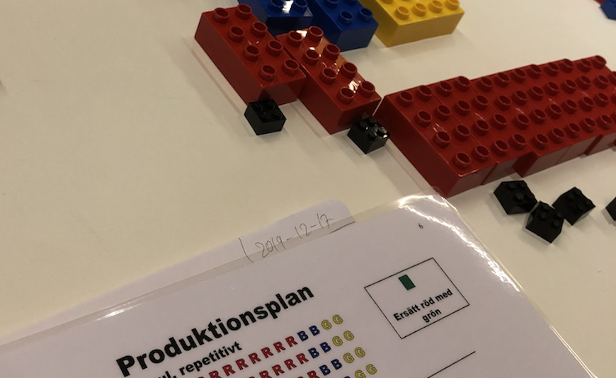 En produktionsplan för LEAN-spel i nederkant av fotot och Lego-klotsar i över kant.