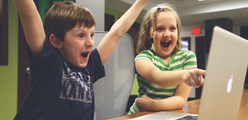En pojke som sträcker upp armarna i luften och en flicka som pekar glatt på en bärbar dator.