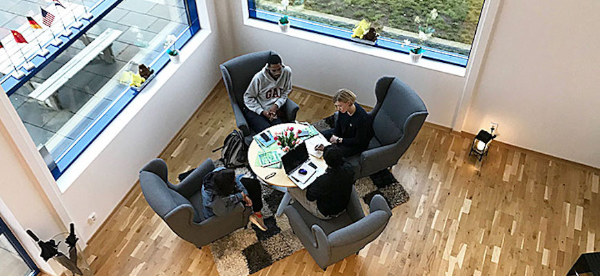 Fotografi från ovan där fyra studenter sitter vid ett runt bord och samtalar. En student har en dator på bordet.