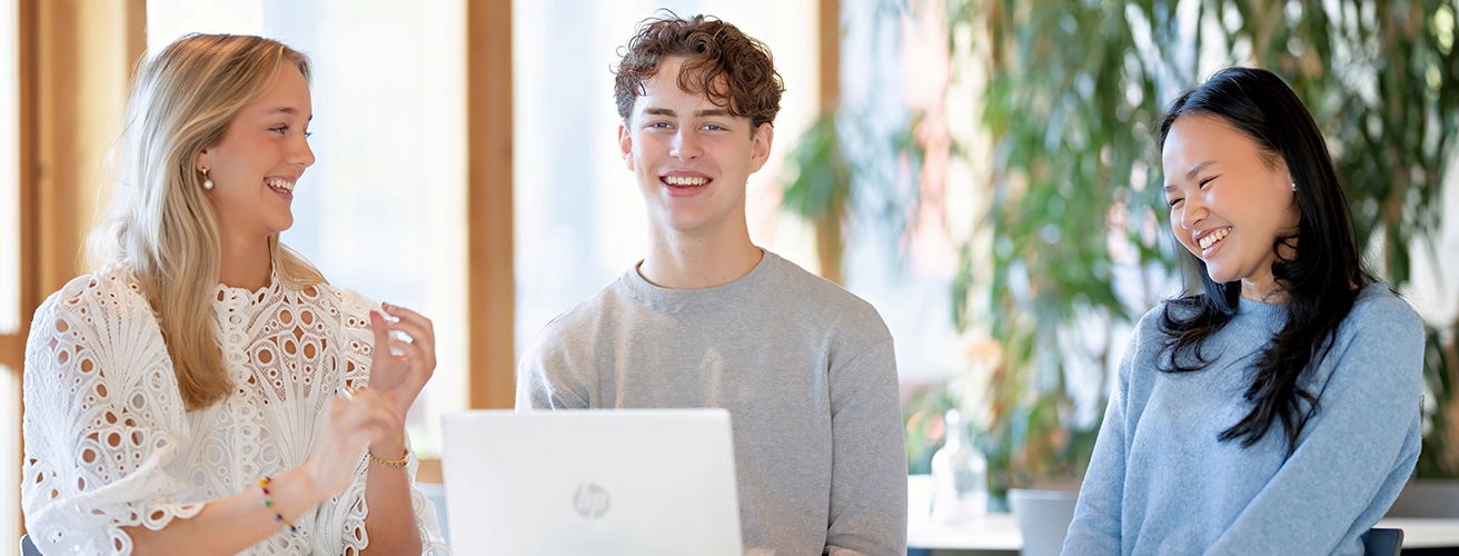 Bild som föreställer fyra elever som sitter tillsammans vid ett bord med en bärbar dator