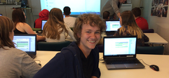 En sal med elever som programmerar och en leende elev tittar in i kameran